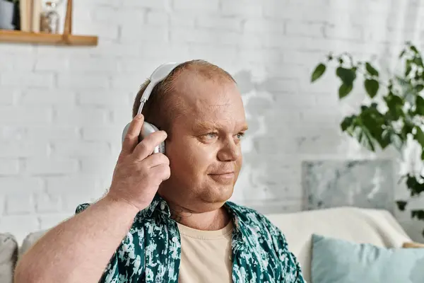 stock image A man with inclusivity wearing headphones sits on a couch in a living room.