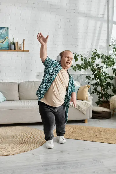 stock image A man with inclusivity in a patterned shirt and jeans dances in a living room.