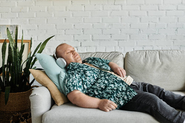 Человек с инклюзивностью расслабляется на сером диване на фоне белой кирпичной стены.