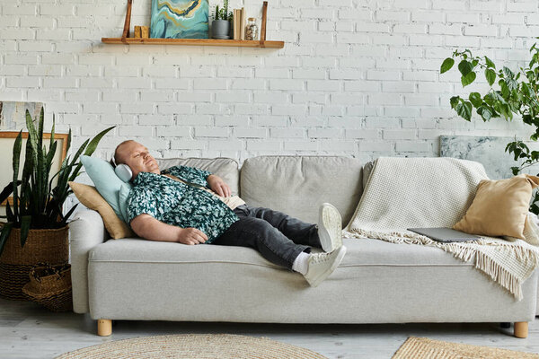 Человек с инклюзивностью мирно покоится на сером диване, одетый в наушники и рубашку с узором.