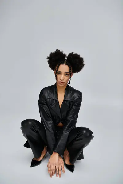 stock image A young African American woman in a black leather jacket and pants poses against a grey background.