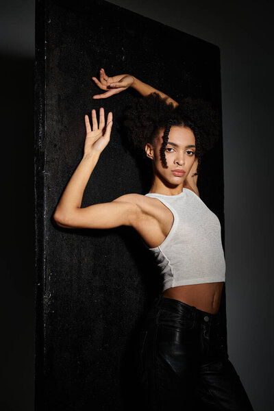 Стильная молодая женщина в белом топе позирует на сером фоне.