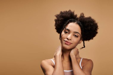 Afro saçlı, güzel bir Afro-Amerikalı kadın bej arka planda poz veriyor.