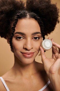 Işıl ışıl gülümseyen genç bir Afrikalı Amerikalı kadın bir krema kavanozu tutuyor ve doğal güzelliğini vurguluyor..