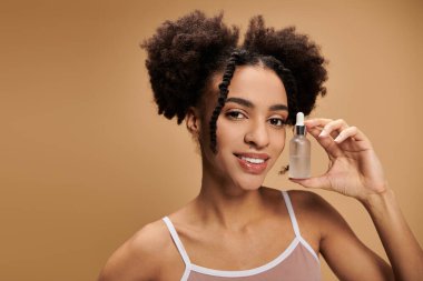 Genç bir Afrikalı Amerikalı kadın bej arka planda bir şişe serum tutarken gülümsüyor..