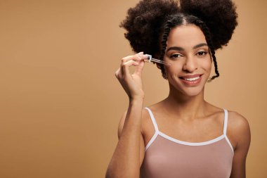 Güzel bir Afro-Amerikalı kadın yüzüne serum sıkarken gülümsüyor..