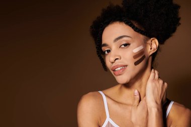 A young African American woman with a warm smile stands against a beige background, showcasing different skin tones on her cheek. clipart