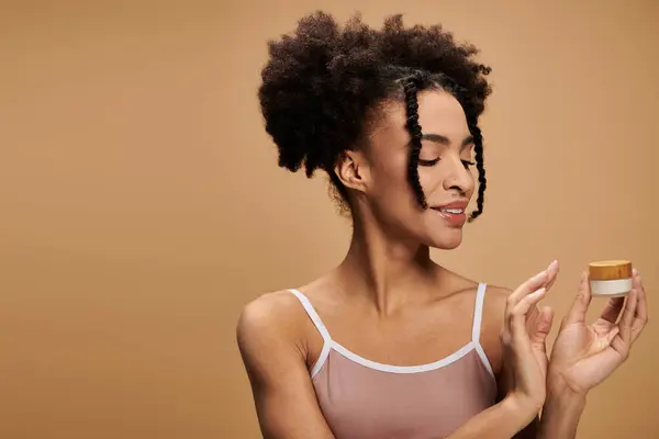 stock image A young African American woman with a radiant smile holds a cream jar, showcasing her natural beauty and confidence.