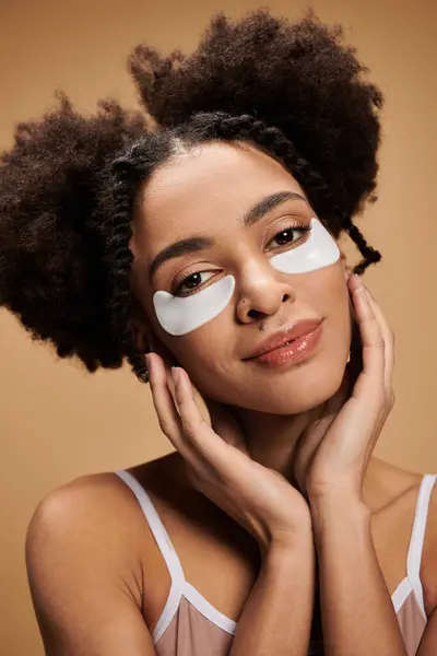 stock image A young woman with curly hair and under-eye patches rests her hands on her face, looking calmly at the camera.