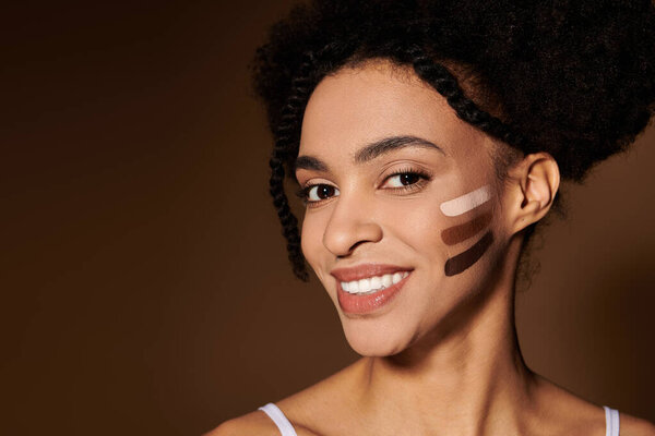 A young African American woman smiles confidently with makeup swatches on her cheek, celebrating diversity and beauty in all shades.