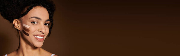 A young African American woman smiles confidently as she models makeup swatches on her cheek.