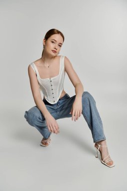 Beyaz korse ve kot pantolon giyen genç bir kadın şık ve kendinden emin görünüyor..