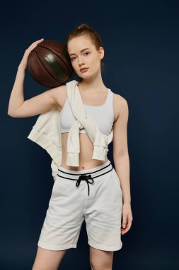 Beyaz spor elbiseli genç bir kadın basketbol topuyla cesur mavi bir zemine karşı poz veriyor..