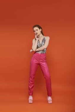 Pembe takım elbiseli genç bir kadın parlak turuncu bir arka plana karşı poz veriyor..