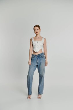 Genç bir kadın beyaz korse ve mavi kotla poz veriyor..