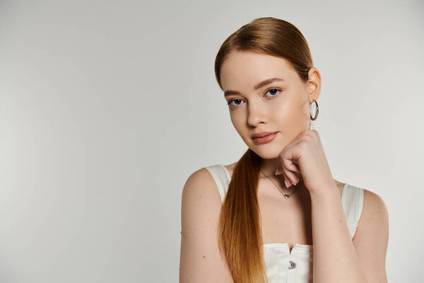 Woman with long red hair poses against white backdrop, hand on chin.