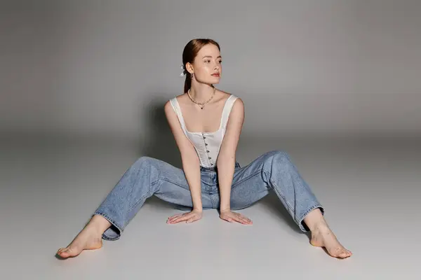 stock image A young woman poses gracefully in loose-fitting denim and a white top against a simple backdrop.