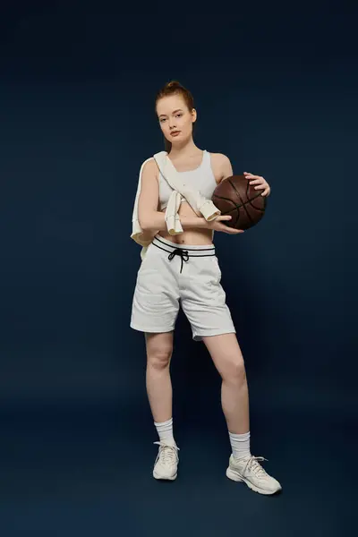 stock image A young woman wearing white shorts and a white sports bra poses with a basketball in her hands.