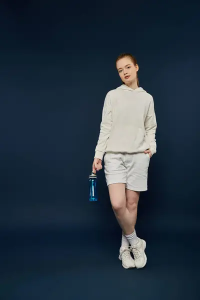 stock image Woman in white hoodie and shorts poses with water bottle against blue backdrop.