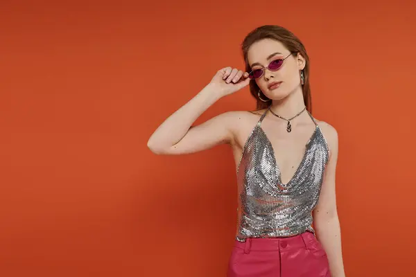 Stock image Young woman confidently poses in front of orange background in silver top.