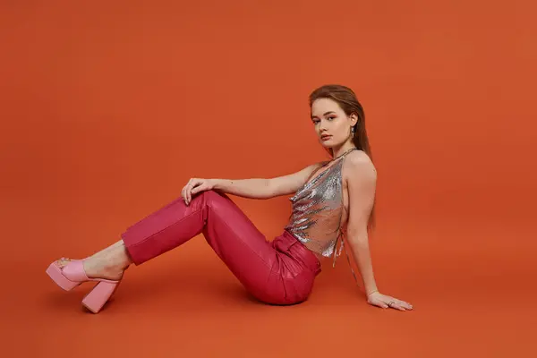 stock image Young woman peacefully sits with legs crossed on vibrant backdrop.