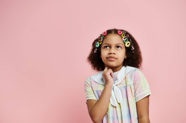 A Black girl with colorful hair clips stands in a pastel dress against a pink backdrop, her thoughtful gaze invoking wonder. clipart