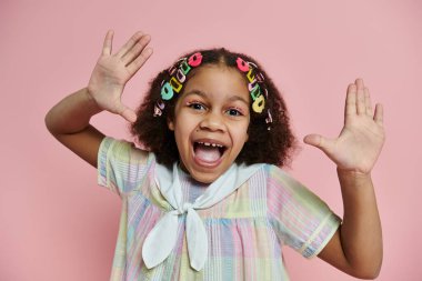 Renkli saç tokasıyla genç bir Afrikalı Amerikalı kız pastel bir elbise giyerken parlak bir şekilde gülümsüyor..