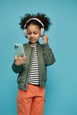 Kıvırcık saçlı genç bir Afrikalı Amerikalı kız elinde akıllı bir telefonla kulaklıkla müzik dinliyor..
