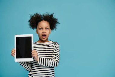 Kıvırcık saçlı genç bir Afro-Amerikalı kız yüzünde şaşırmış bir ifadeyle bir tablet tutuyor..