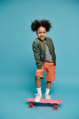 Pembe bir kaykayın üzerinde mavi bir arka planda duran kıvırcık saçlı genç bir Afrikalı Amerikalı kız gülümsüyor..