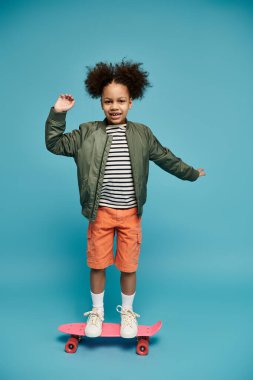 Pembe bir kaykayın üzerinde mavi bir arka planda duran kıvırcık saçlı genç bir Afrikalı Amerikalı kız gülümsüyor..