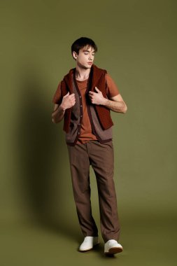 Kahverengi yelekli bir adam parlak yeşil bir zemine karşı poz verir..