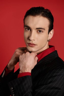 A man in a black suit and red shirt poses against a vibrant red backdrop. clipart