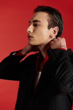 Siyah takım elbiseli bir adam canlı kırmızı bir arkaplanda poz veriyor..