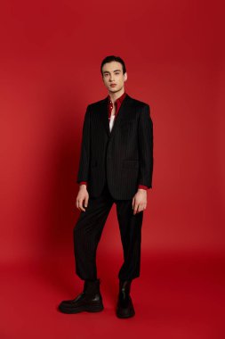 A man in a black pinstripe suit stands against a bold red backdrop, exuding confidence and style. clipart