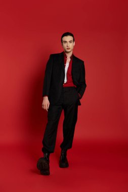 A man in a black suit stands against a red background. clipart