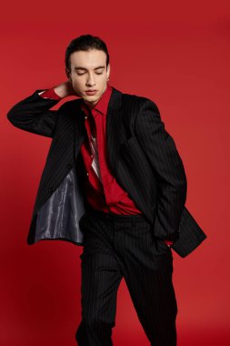 A man in a black suit poses against a red backdrop. clipart