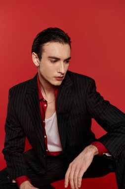 Siyah çizgili takım elbiseli bir adam kırmızı bir arkaplanda poz veriyor..