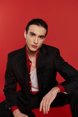 Siyah takım elbiseli bir adam canlı kırmızı bir arkaplanda poz veriyor..