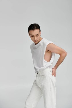 Beyaz atletli ve kot pantolonlu bir adam beyaz bir fonda poz veriyor..