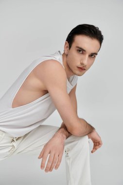 Beyaz atletli ve pantolonlu genç bir adam beyaz bir arkaplanda poz veriyor..