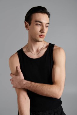 A young man poses against a simple gray background, wearing a black tank top and a gold chain. clipart