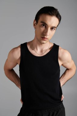 A handsome man in a black tank top poses against a gray backdrop, exuding confidence and style. clipart