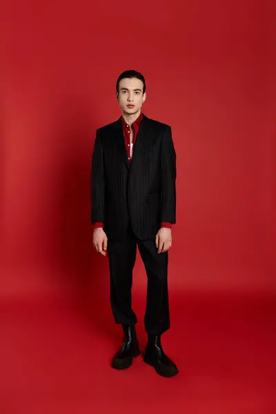 stock image A man in a black suit stands confidently against a vibrant red backdrop.