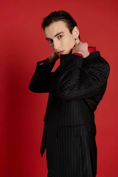 stock image A man in a black suit with white stripes poses against a red backdrop.