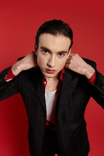 A handsome man in a black pinstriped suit poses with a hint of red peeking out from his collar.