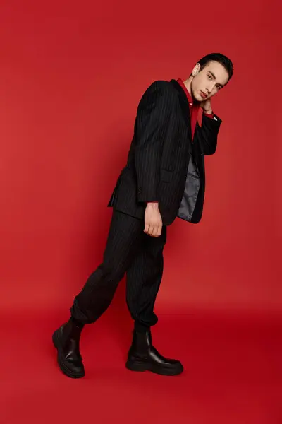 stock image A man in a black suit walks confidently on a vibrant red backdrop.