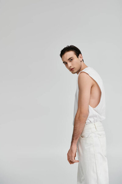 A stylish man poses in a white tank top and pants against a white background.