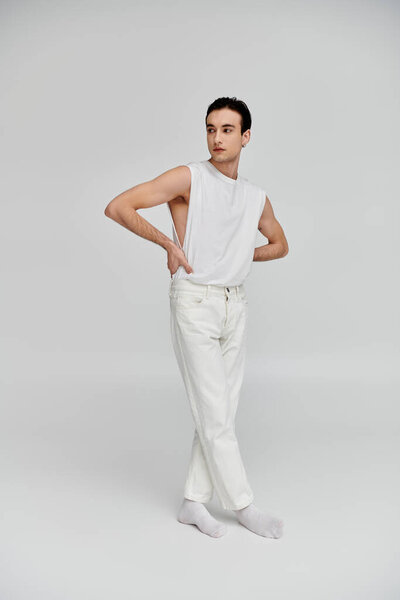 A handsome man in a white tank top and jeans poses against a white background.