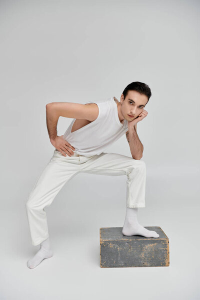 A man in white clothing poses on a grey box against a white background.